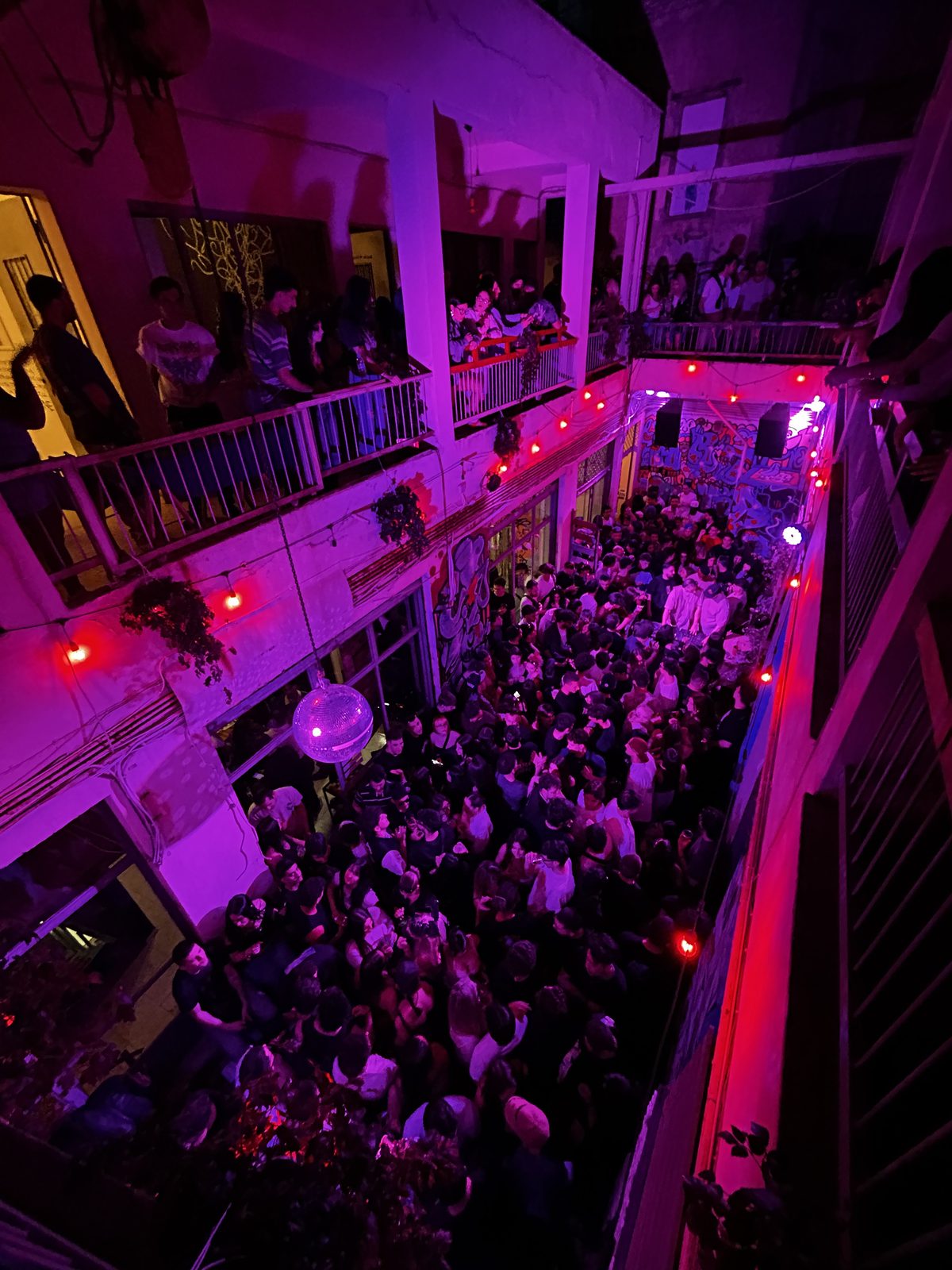 ARTHINA — courtyard packed with visitors under disco lights and red bulbs