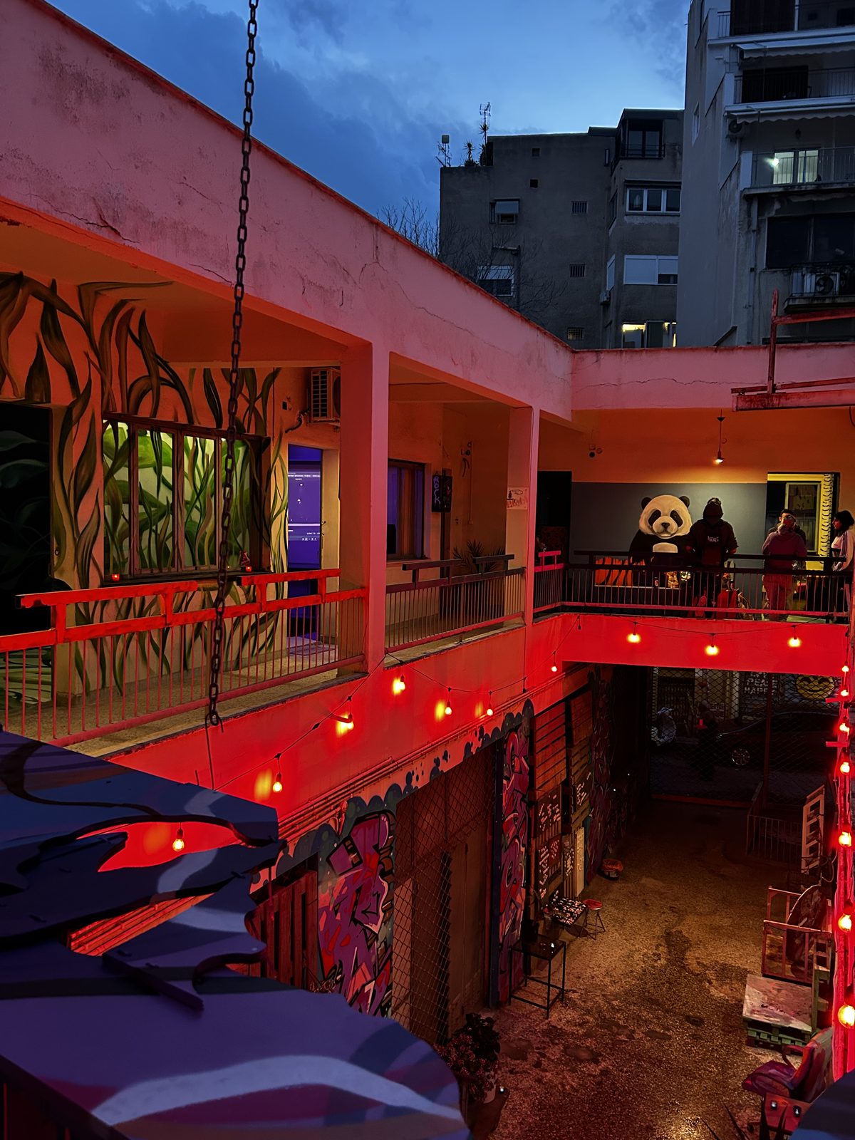 ARTHINA courtyard at dusk — red string lights, graffiti, mascot